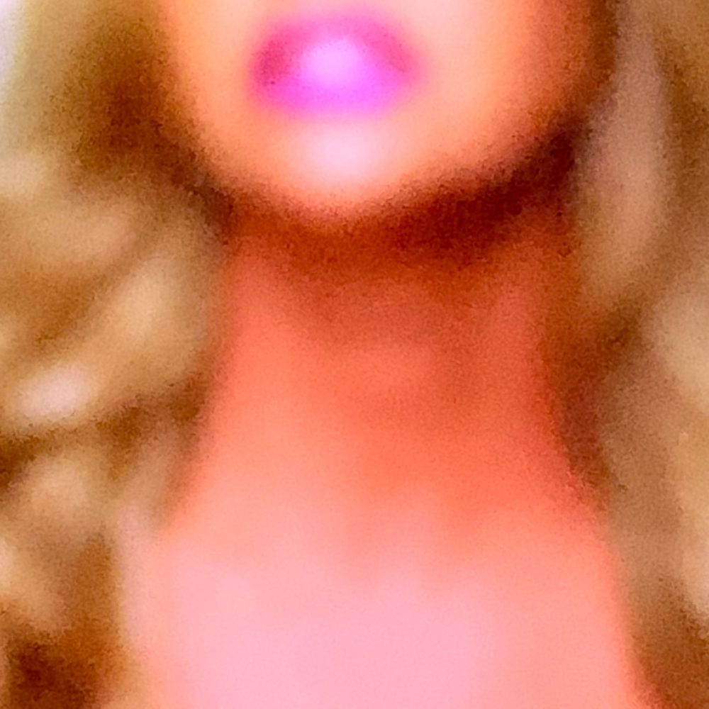 Close-up of a woman with long blonde hair and bright pink lips against a warm glowing background.