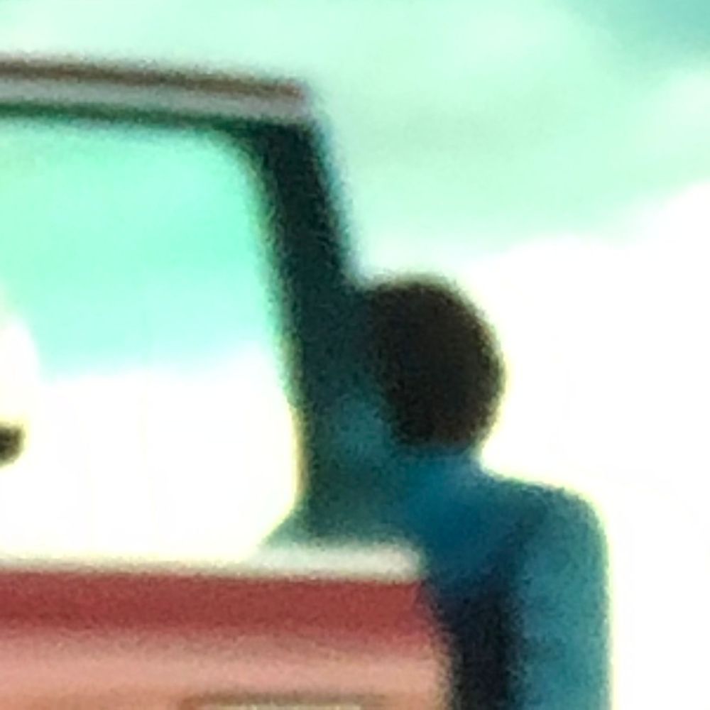 Silhouette of a person standing beside a teal vehicle door against a bright sky background.