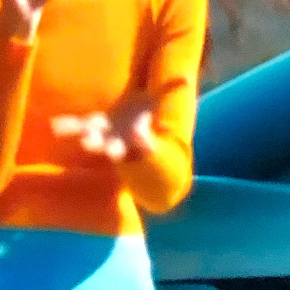 Person in orange jacket holding small object near teal surface, blurred close-up shot.