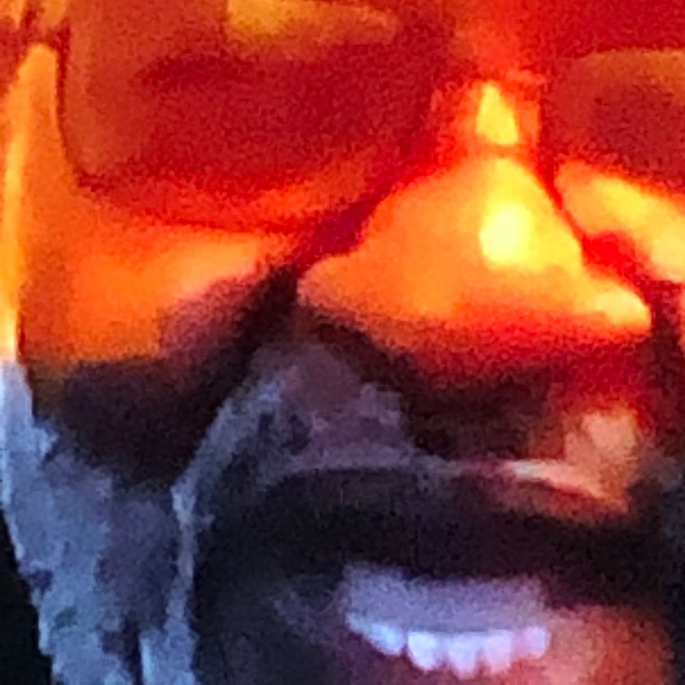 Close-up of a smiling man with a beard wearing orange-tinted sunglasses with warm light reflections.