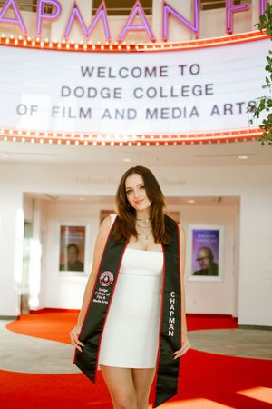 Female graduate in white dress with Chapman Dodge College of Film and Media Arts stole.