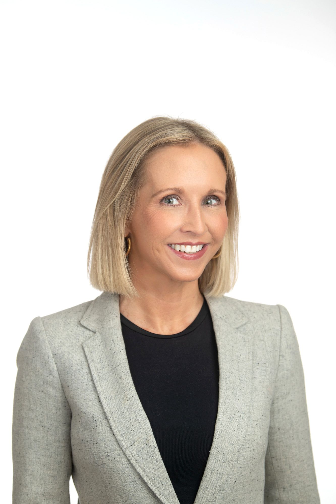 Professional woman in gray blazer and black top smiling confidently against white background.