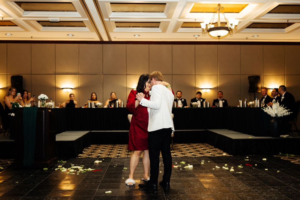 Couple sharing first dance at wedding reception in elegant ballroom with guests seated at head table.