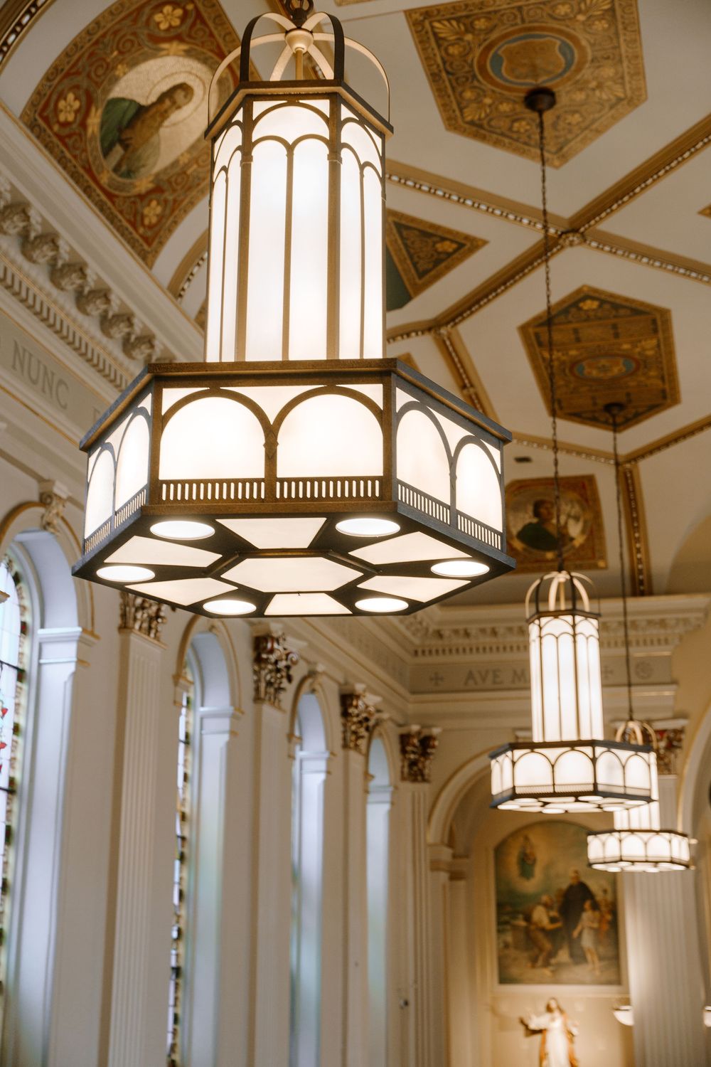 Ornate church interior featuring elegant hexagonal pendant lanterns with arched details and gilded coffered ceiling.