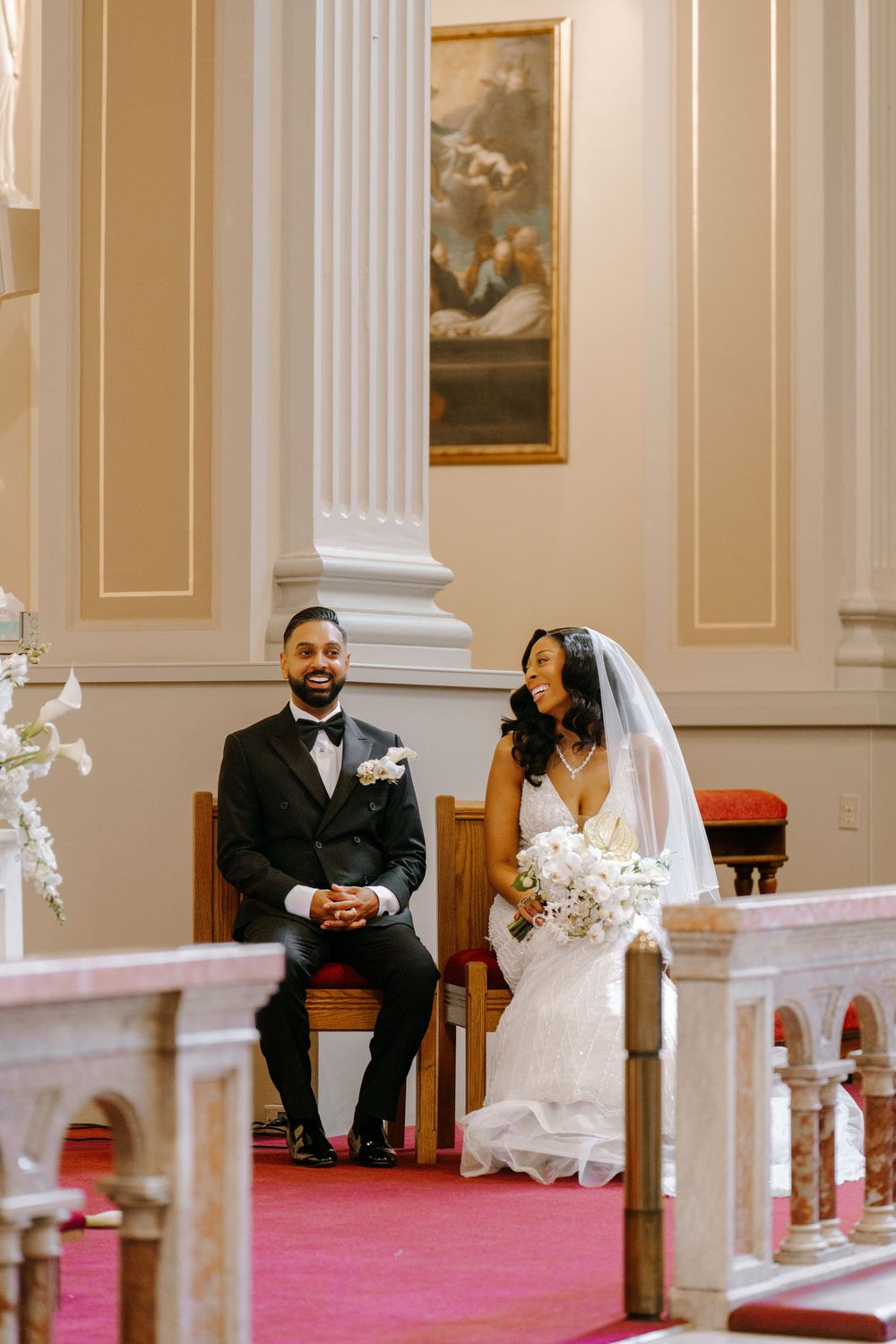 A bride and groom sit together at the altar during their elegant church wedding ceremony, smiling joyfully.