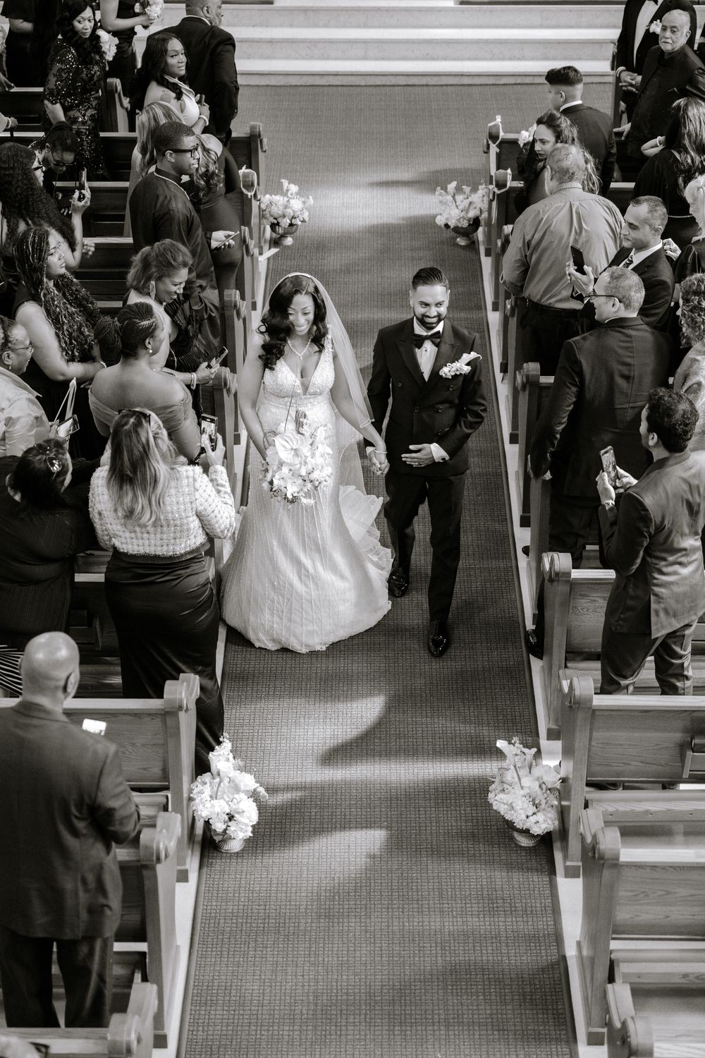 Black and white photo of bride and groom walking down church aisle after wedding ceremony.