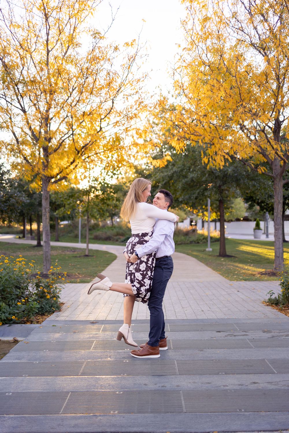 Couple embracing on a park pathway surrounded by golden autumn trees at sunset.