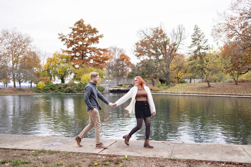 Couple holding hands walking by a pond in Eden park in Cincinnati during autumn, surrounded by colorful fall foliage.