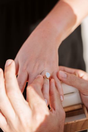 Close-up of an engagement ring being placed on a woman's finger, featuring a large oval diamond in a gold setting.