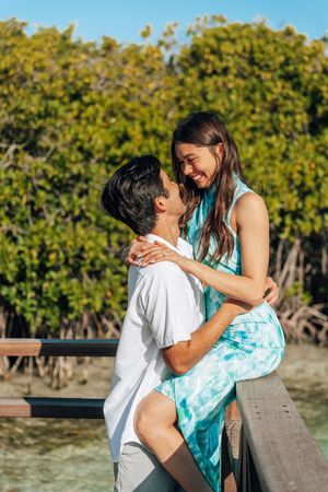 Romantic couple embracing on a wooden dock surrounded by lush mangroves and turquoise water on a sunny day.