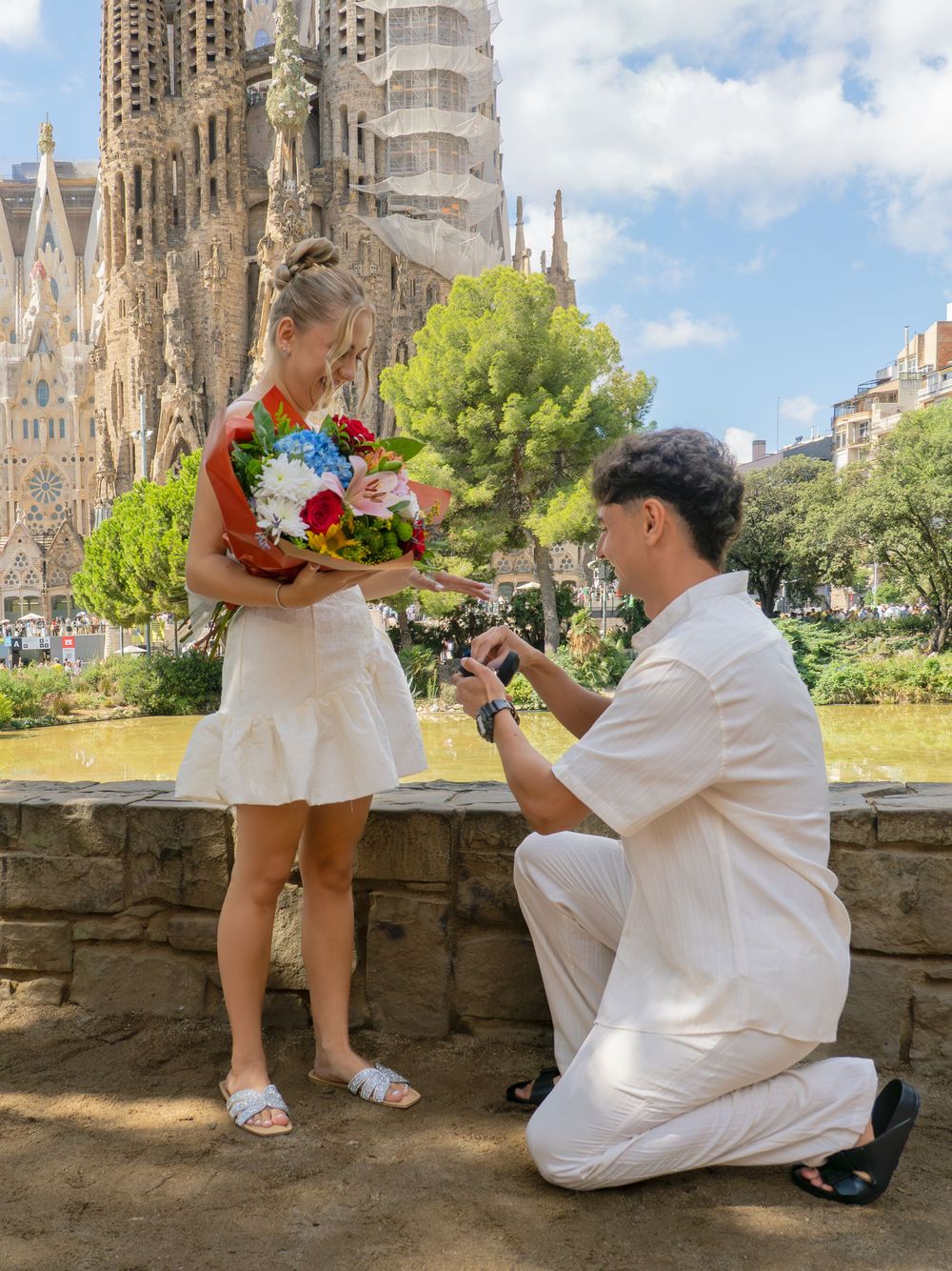 Man proposes to woman holding flowers in front of Sagrada Familia in Barcelona, Spain.