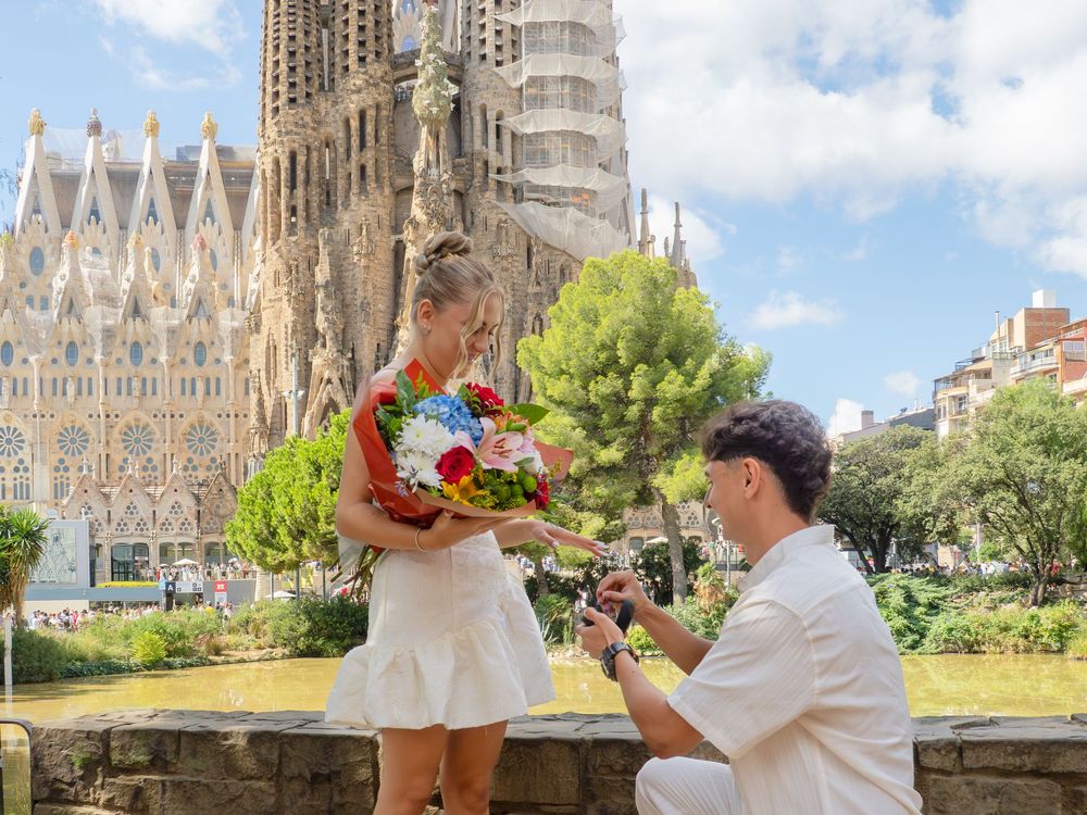 Man proposes to woman holding flowers in front of Sagrada Familia basilica in Barcelona, Spain.
