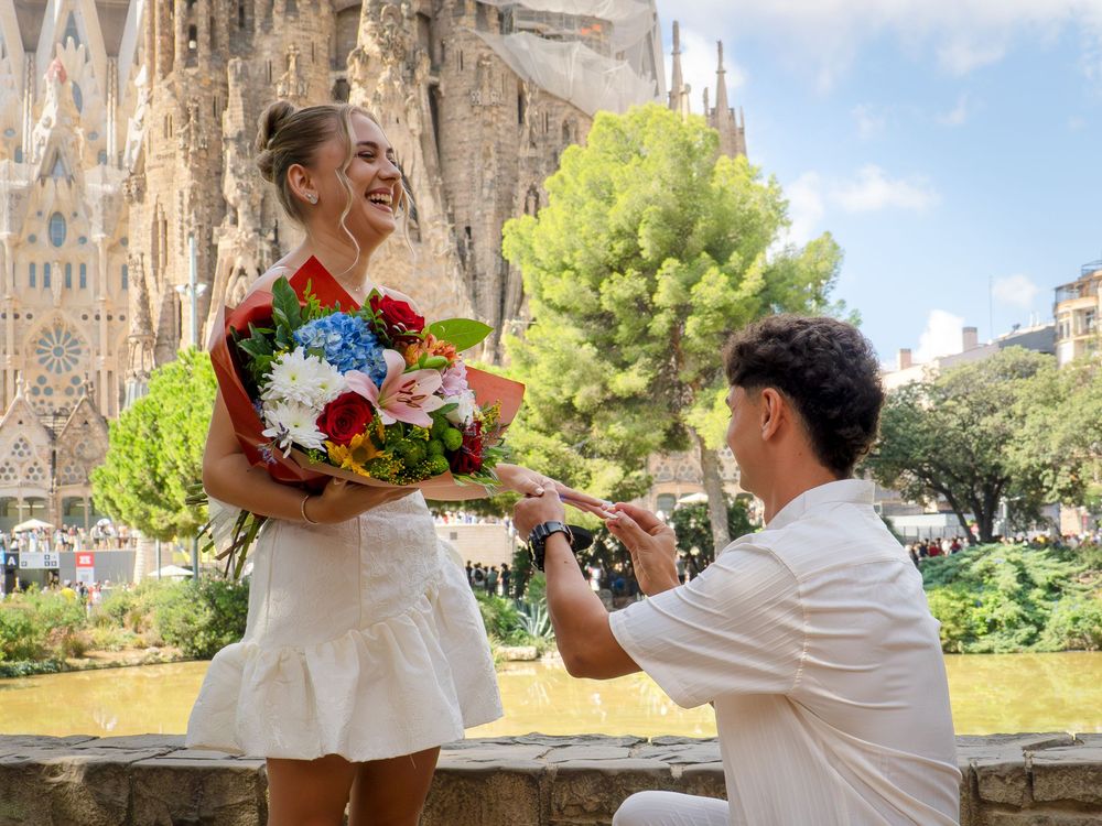 Man proposes to woman with flowers in front of Sagrada Familia in Barcelona on a sunny day.