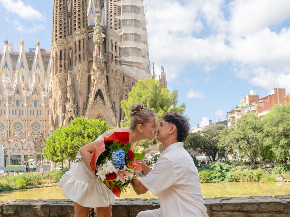Couple sharing a romantic kiss during a marriage proposal in front of the Sagrada Familia in Barcelona, Spain.