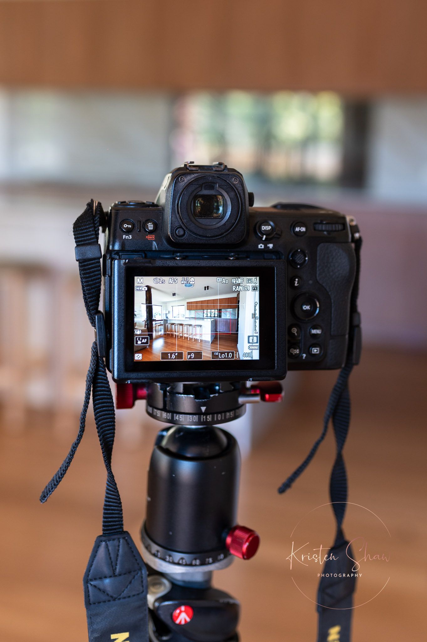 A mirrorless camera on a tripod displays a kitchen interior on its LCD screen during a real estate photography shoot.