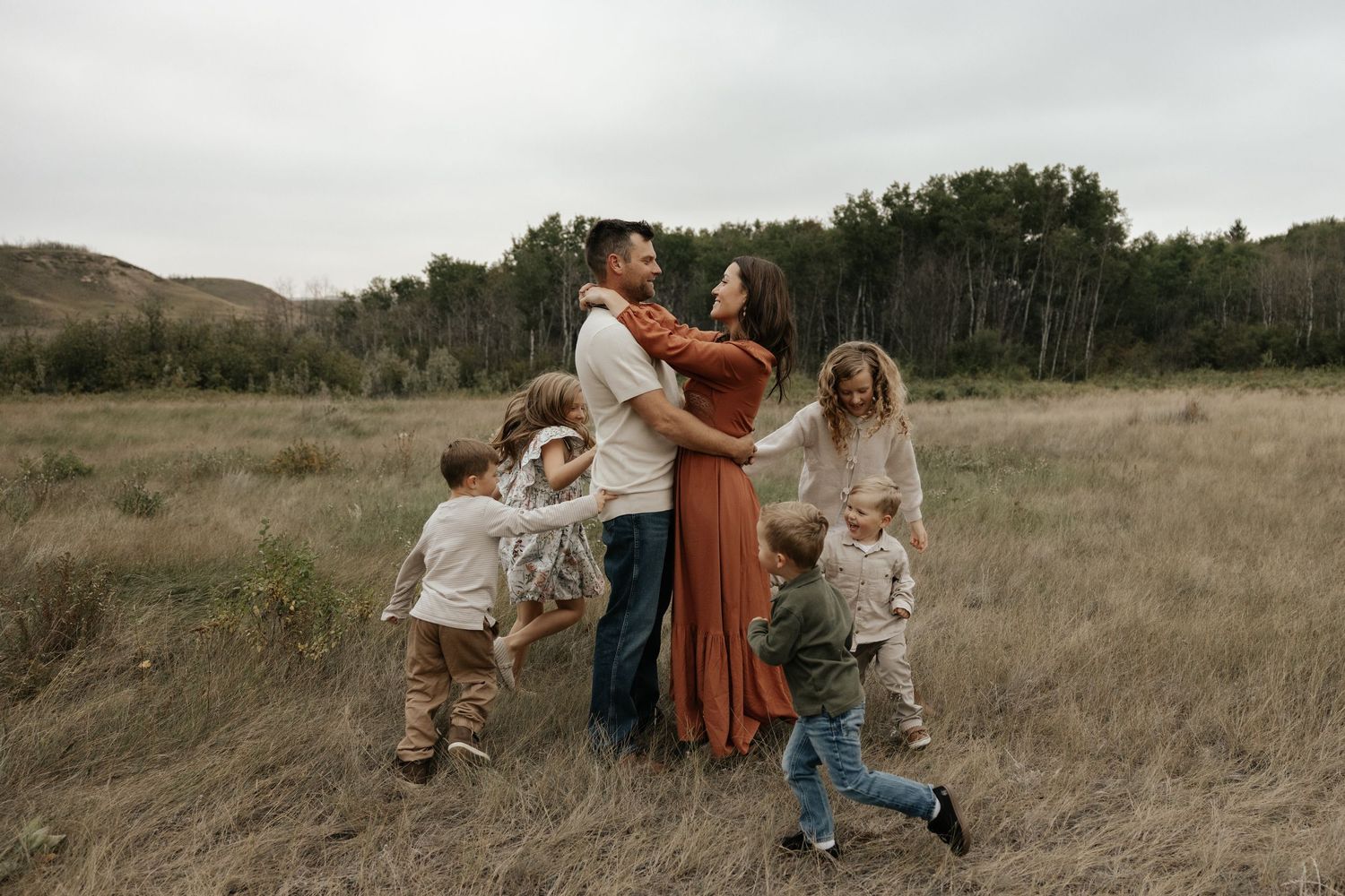 mom and dad embrace while their kids joyfully run around them during a candid family photoshoot in central alberta