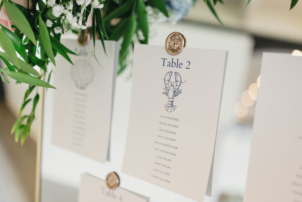 Elegant wedding seating chart cards with gold wax seals displayed on a white board with greenery.
