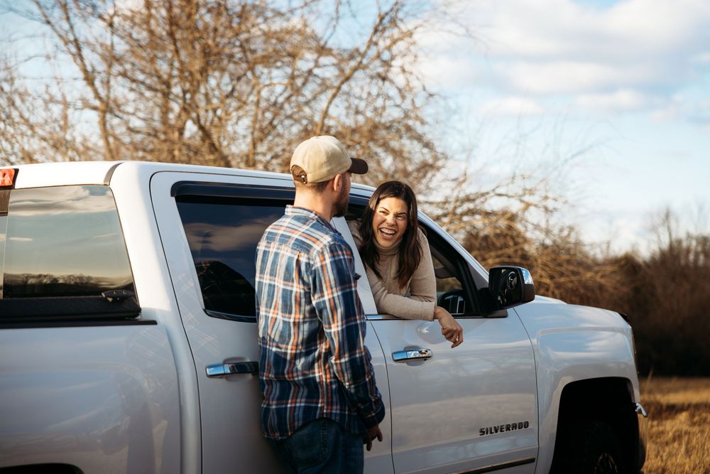 Couple smiling and talking by a white Chevrolet Silverado truck outdoors on a sunny day.