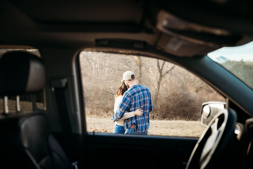 Couple embracing outside a truck in a rural field, viewed through the car window on a sunny day.