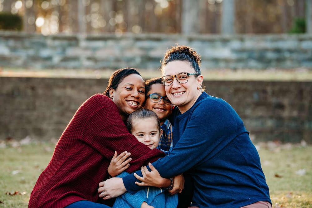 Two women and two children sharing a warm group hug outdoors in a park.