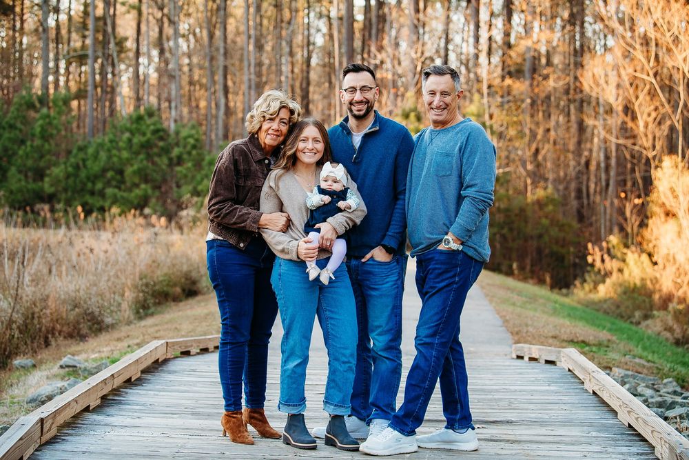 Family of four posing with a small dog on a wooden boardwalk surrounded by trees.