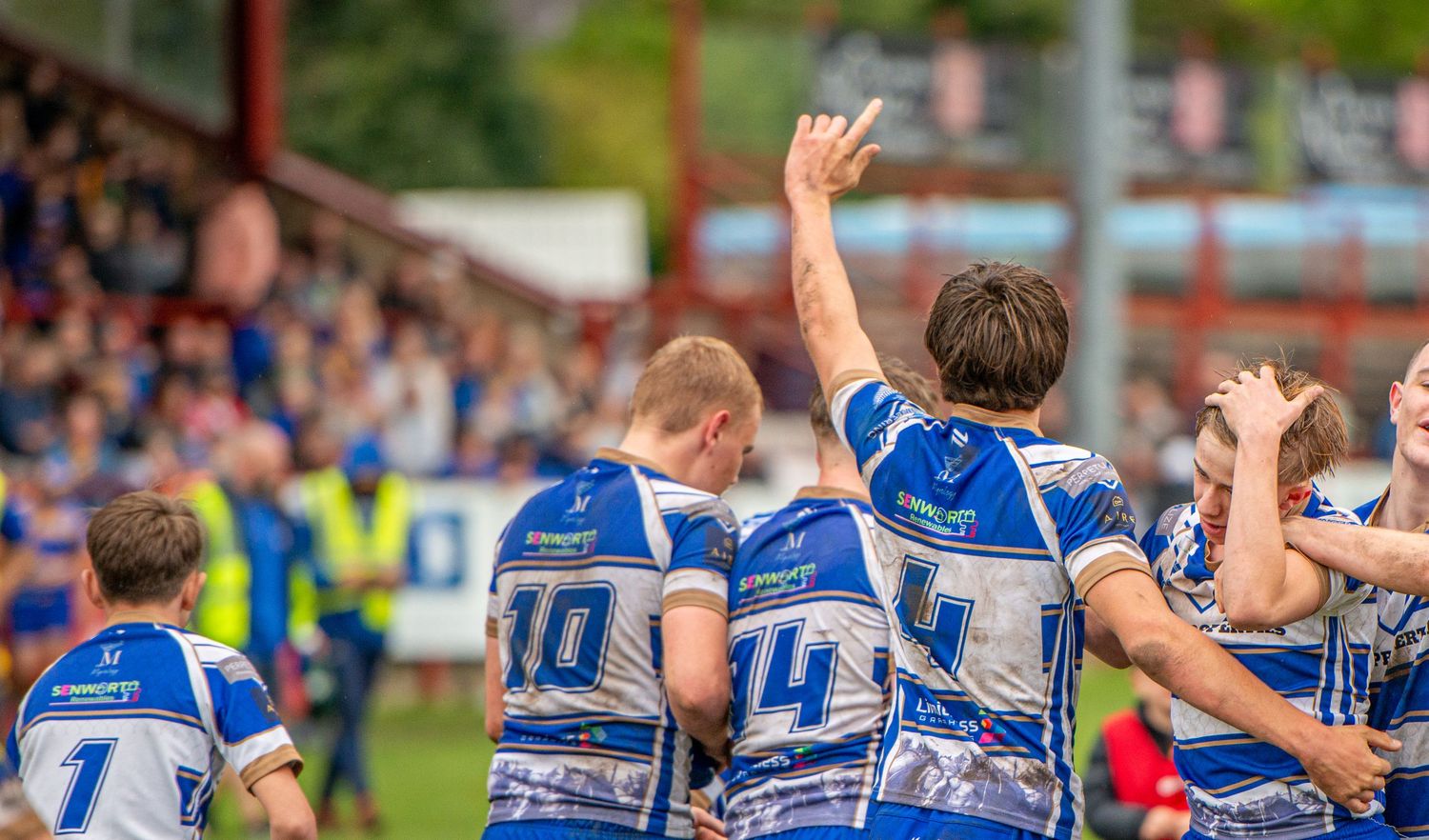 Rugby league players in blue and white jerseys celebrating with raised arm at stadium.