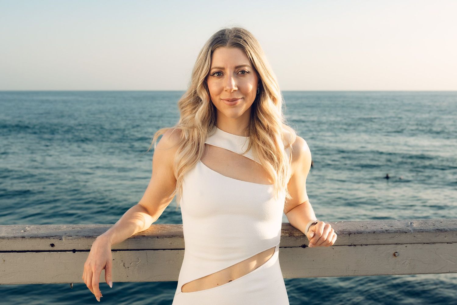 San Diego portrait photography of a woman in a white dress posing by a railing overlooking the ocean waves during golden hour.