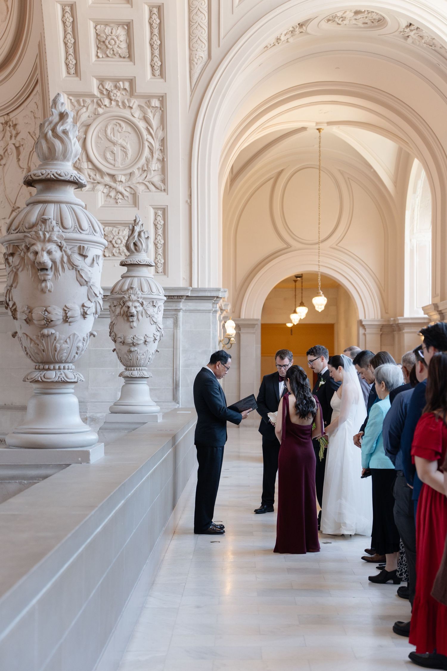 Elegant wedding ceremony in San Francisco City Hall's ornate marble hallway with arched ceilings and decorative urns.
