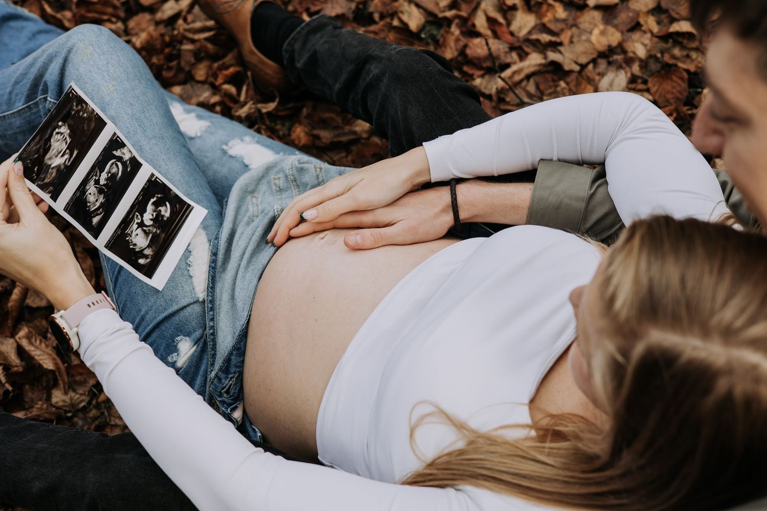 Overhead view of expectant parents holding ultrasound photos while resting hands on a pregnant belly.