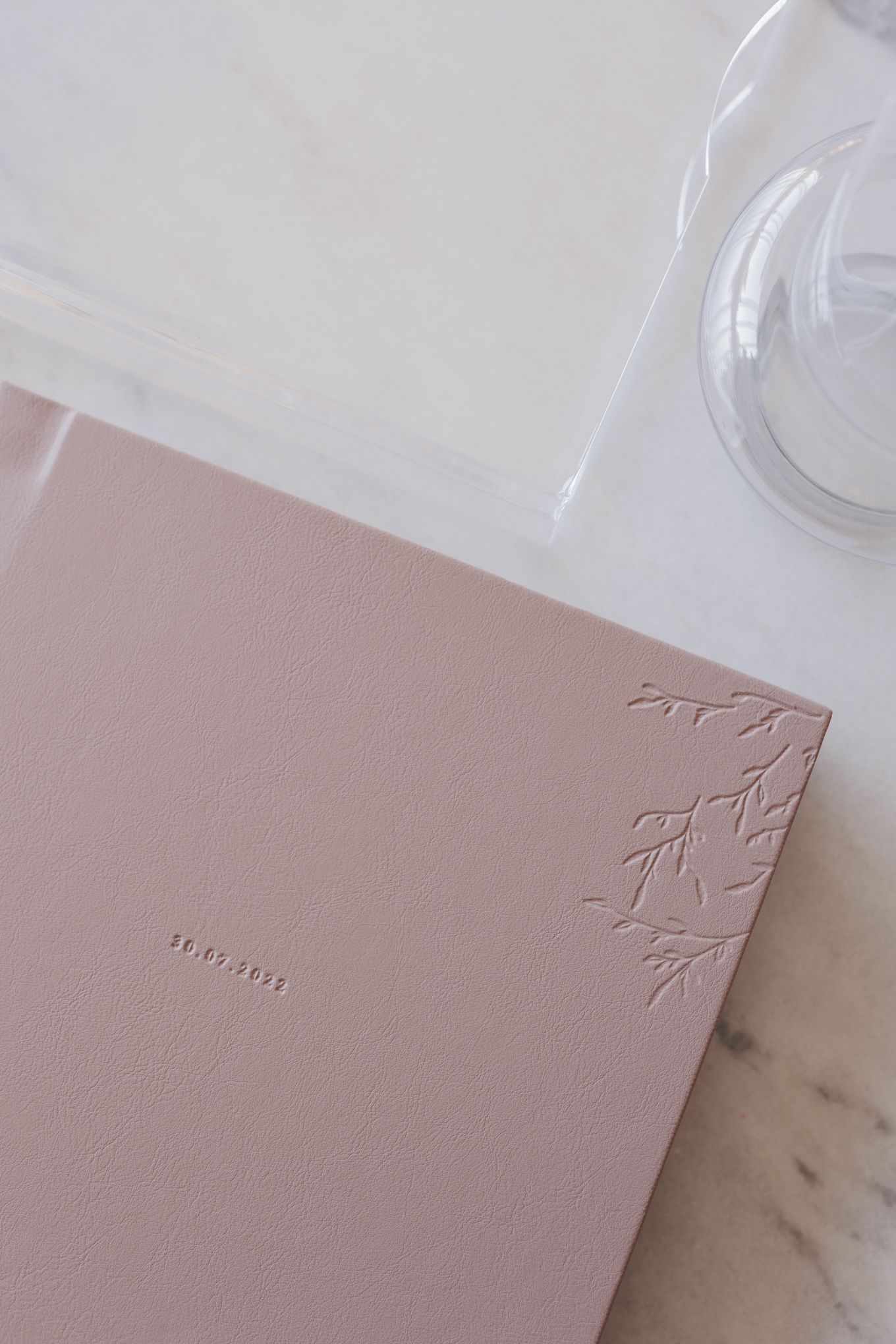 Elegant dusty pink leather journal with embossed floral corner detail and date stamp on marble surface.