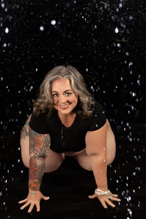 Smiling woman with gray hair and sleeve tattoo posing on black background with falling snow effects.
