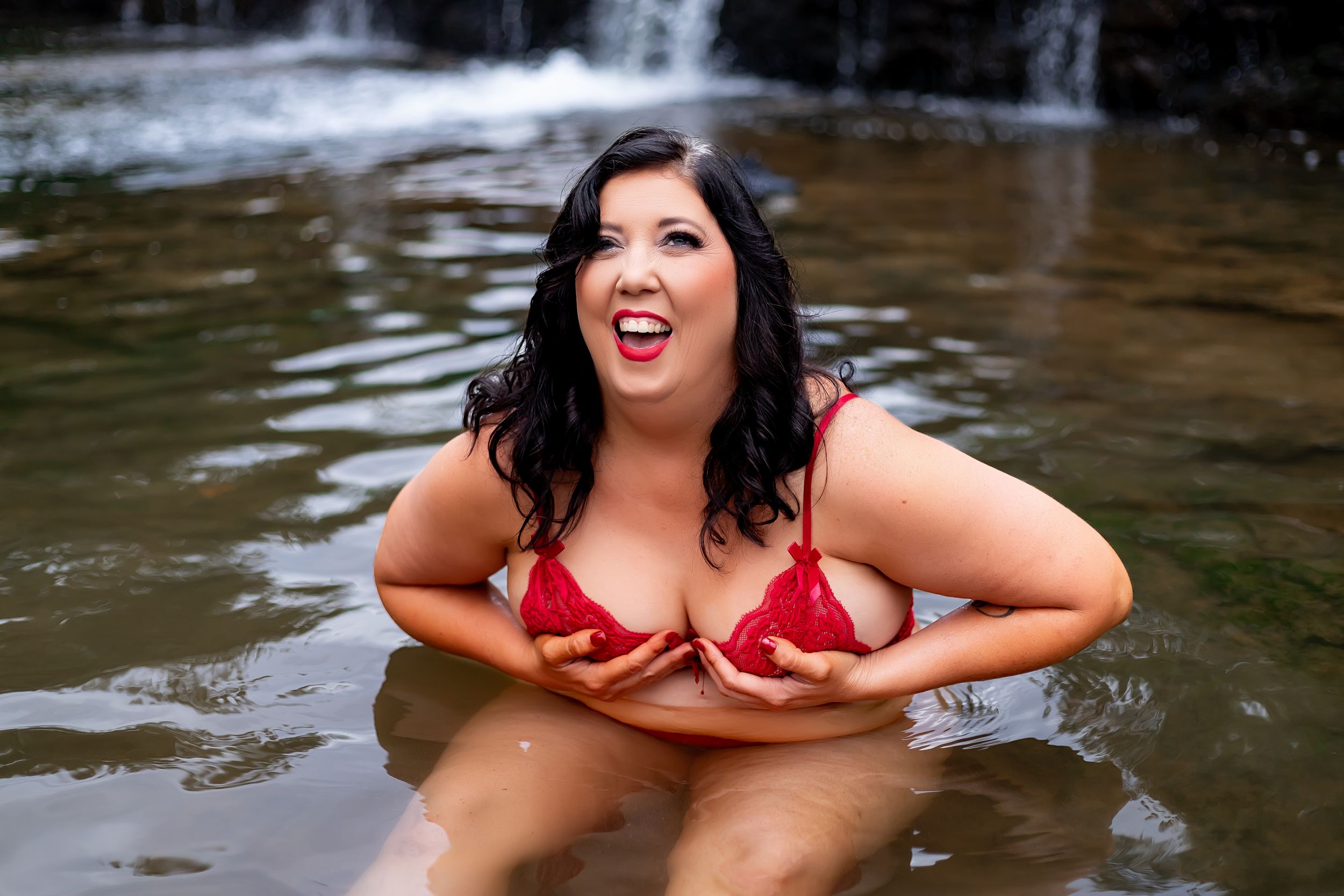 A joyful figure in a red swimsuit laughs while enjoying a swim near a cascading waterfall.