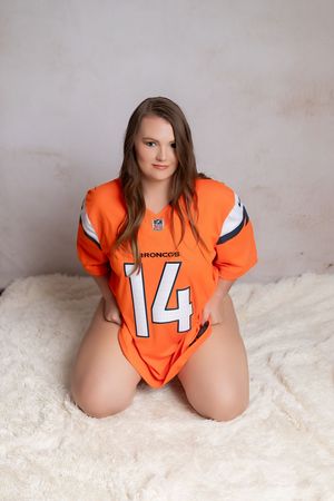 Person wearing orange Denver Broncos football jersey number 14 poses on white fur background.