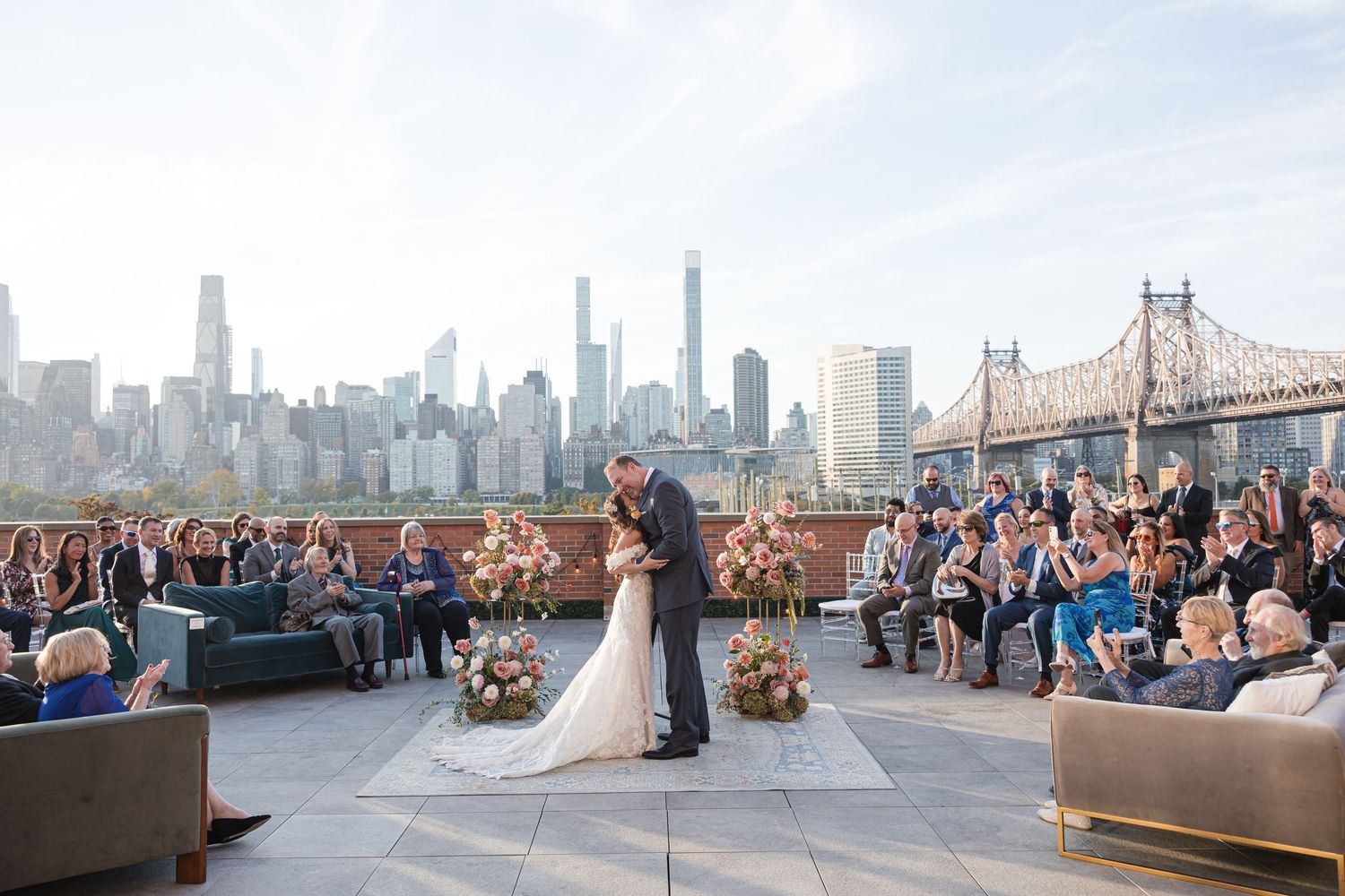 Couple kisses at rooftop wedding ceremony with NYC skyline and Queensboro Bridge backdrop.