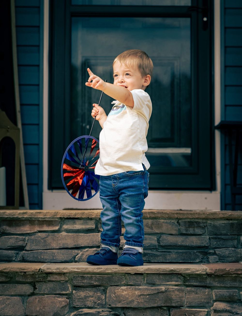 Toddler boy pointing while holding pinwheel on stone steps.