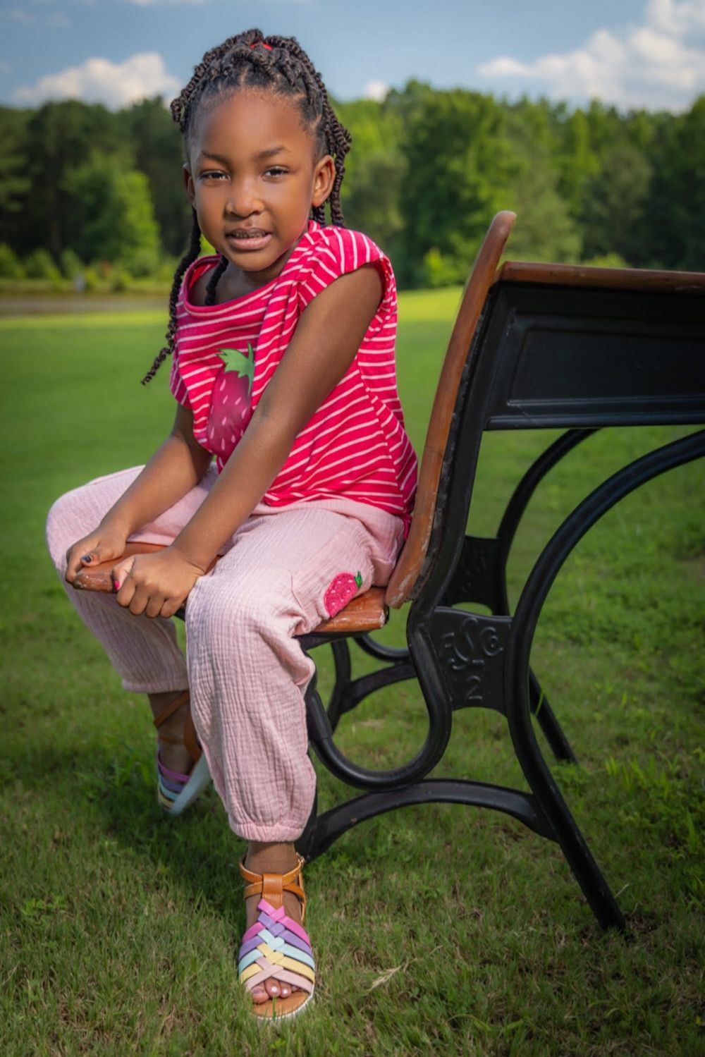 Young girl in pink striped shirt sitting on a park bench outdoors.