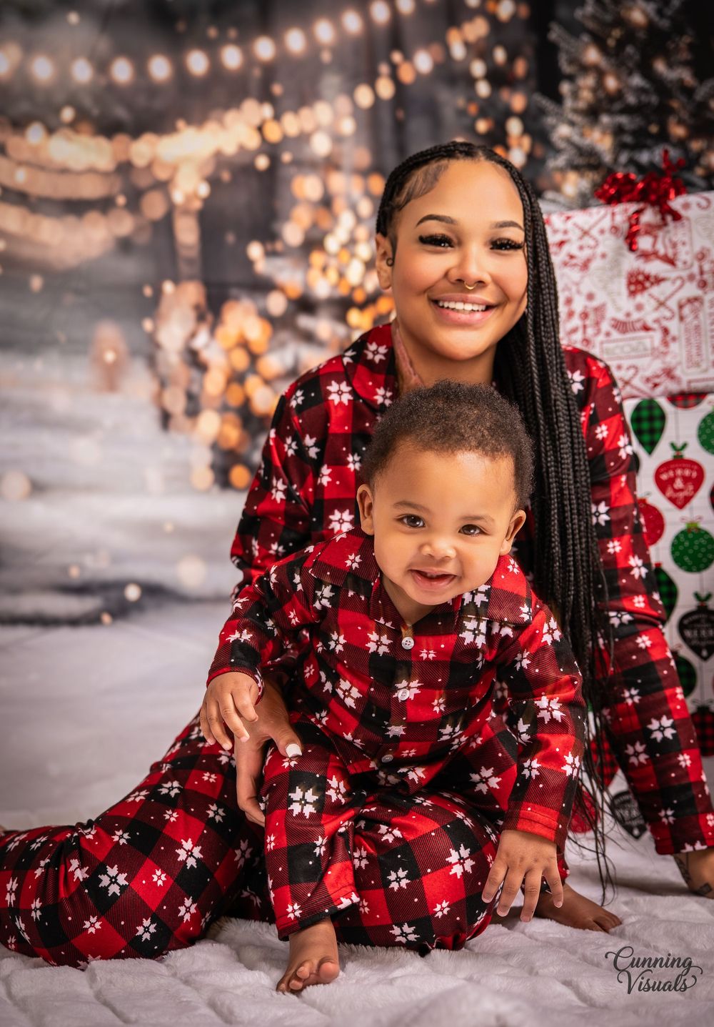 Mother and child in matching red plaid Christmas pajamas posing for a holiday portrait with festive decorations.