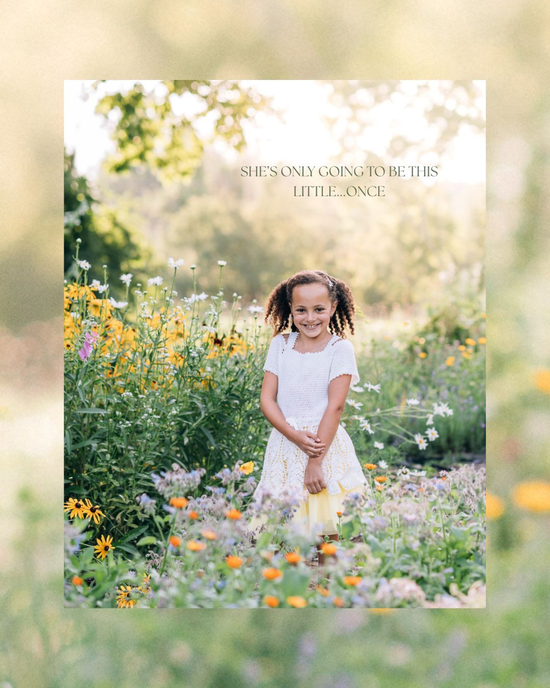 A young girl in a white dress stands smiling among colorful wildflowers in a sunlit garden.