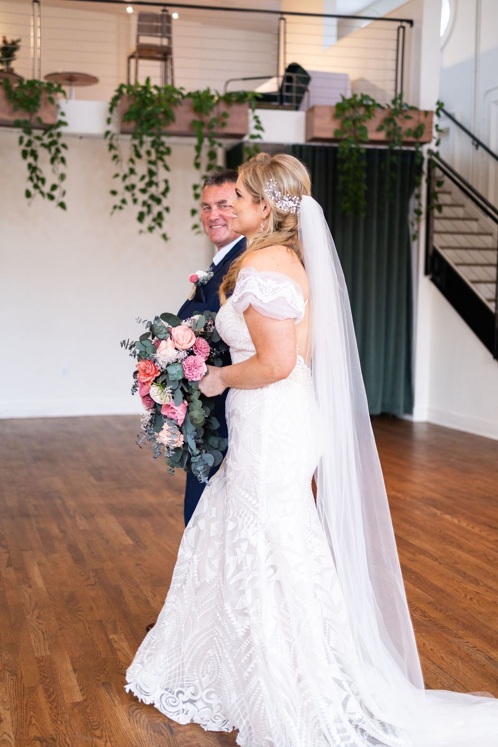 Bride in off-shoulder lace gown with veil holds pink bouquet while walking down the aisle with her dad at the Alcove Cincinnati venue.