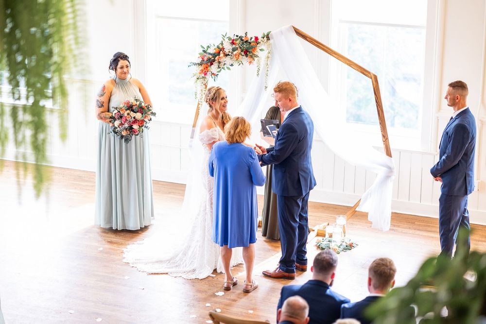 Bride and groom exchange vows under a hexagonal arch with floral decor in a bright indoor wedding ceremony at the Alcove Cincinnati.