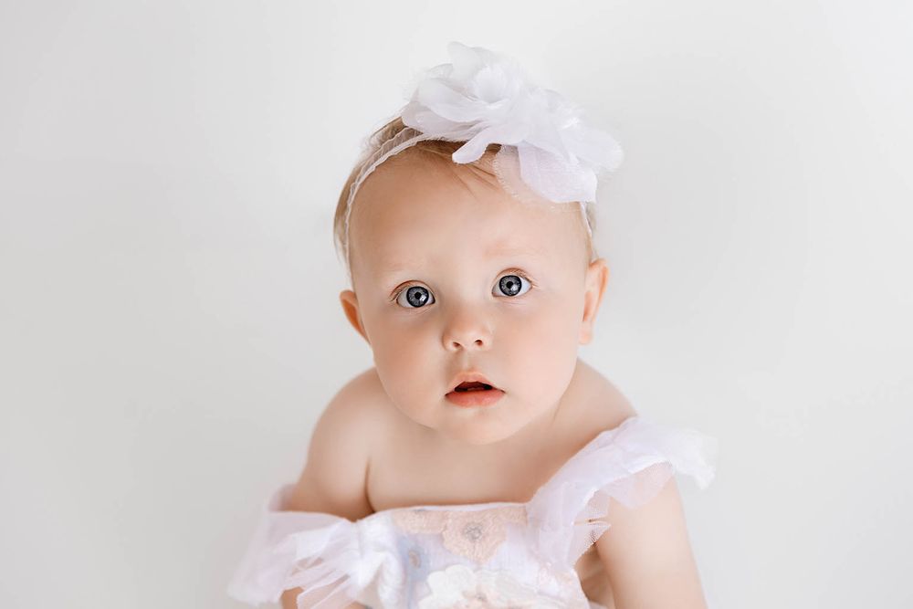 Sweet baby girl with blue eyes wearing a white floral headband and pink tutu dress.