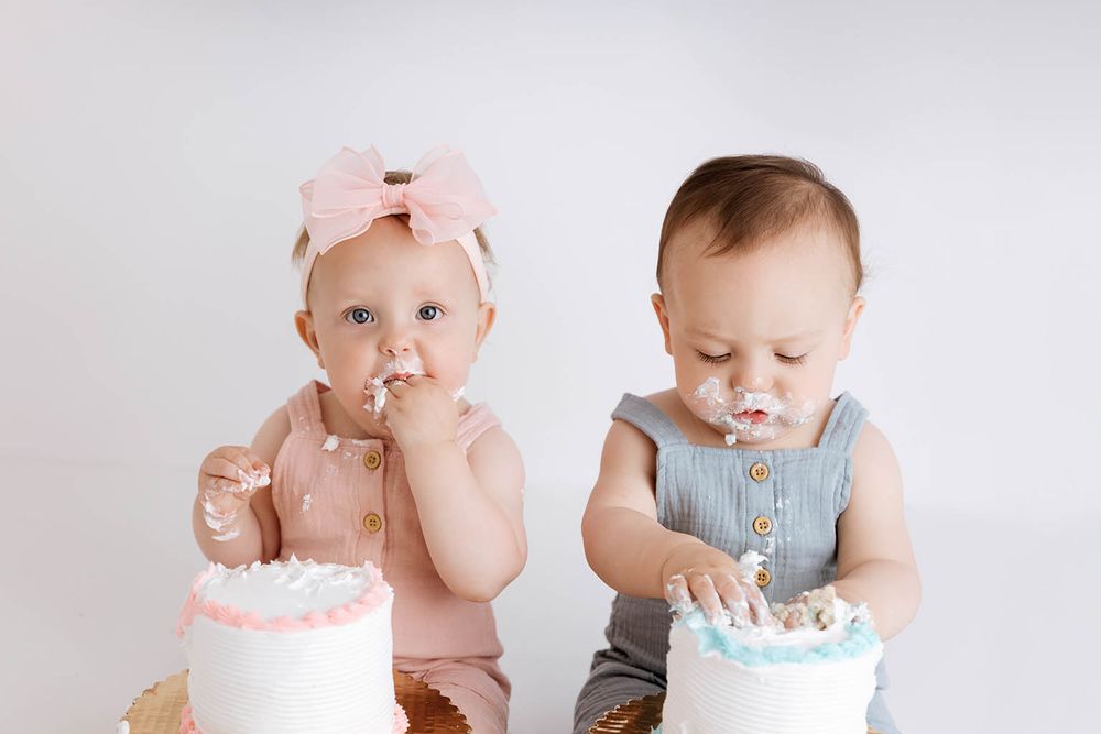 Twin babies enjoying their first birthday cake smash with pink and blue cakes.