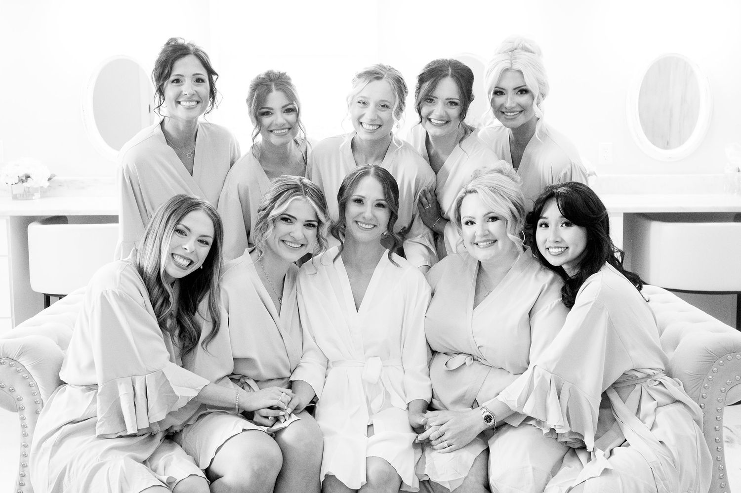 Black and white photo of a bride and her bridesmaids in matching robes smiling together before the wedding ceremony.