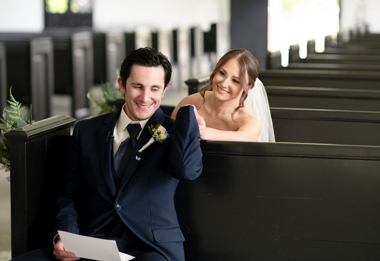 Happy bride and groom sitting in church pews, smiling together on their wedding day.