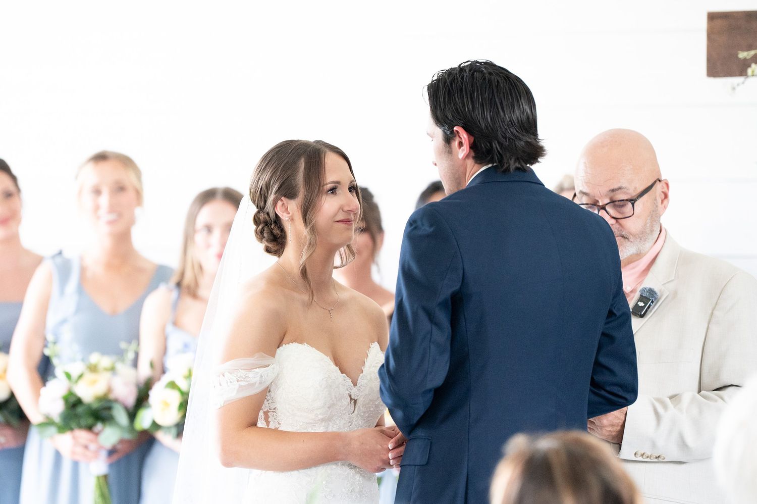 Bride and groom exchange vows at wedding ceremony with bridesmaids in blue dresses standing in background.
