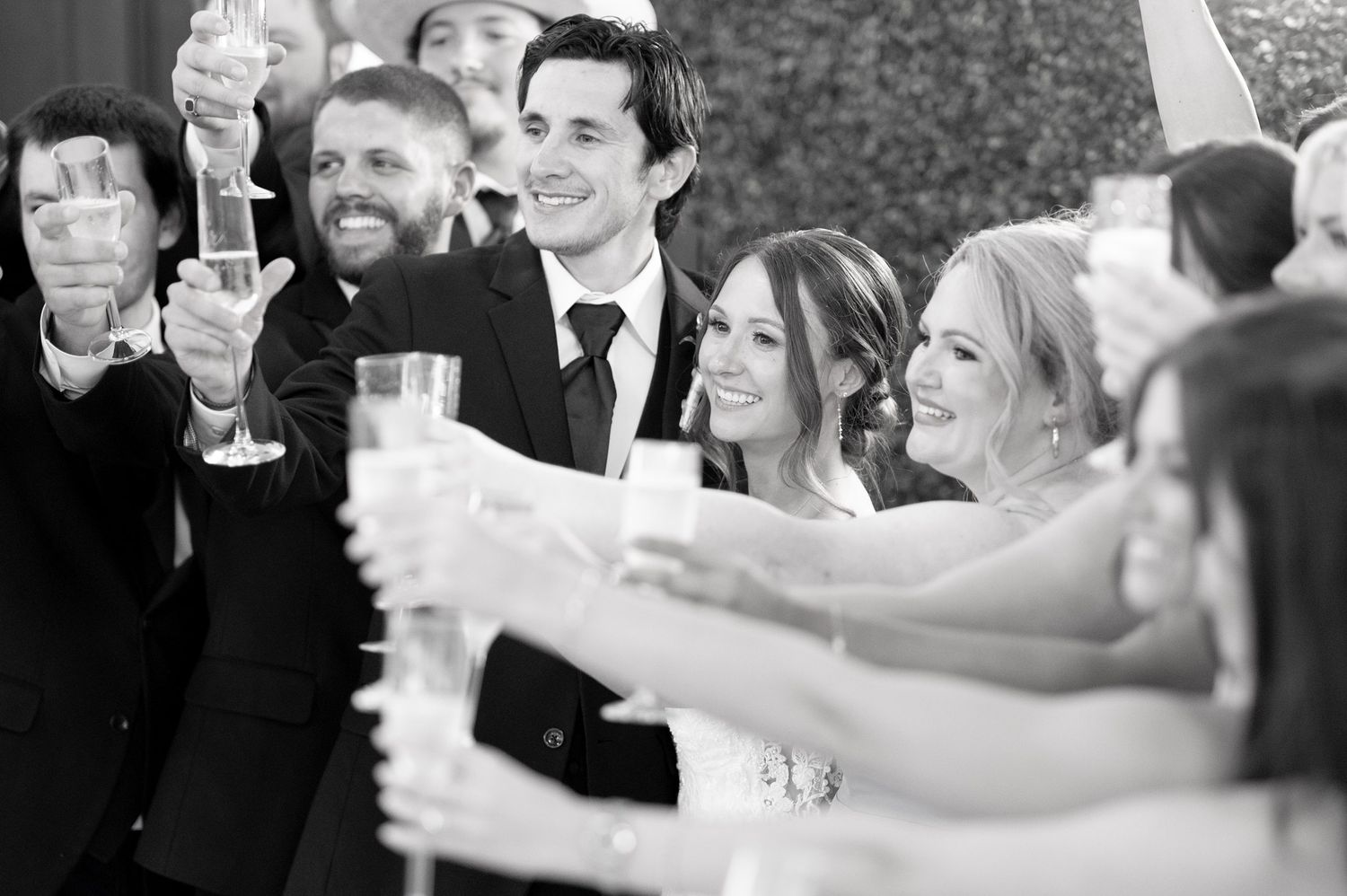 Black and white wedding toast with guests raising champagne glasses in celebration.