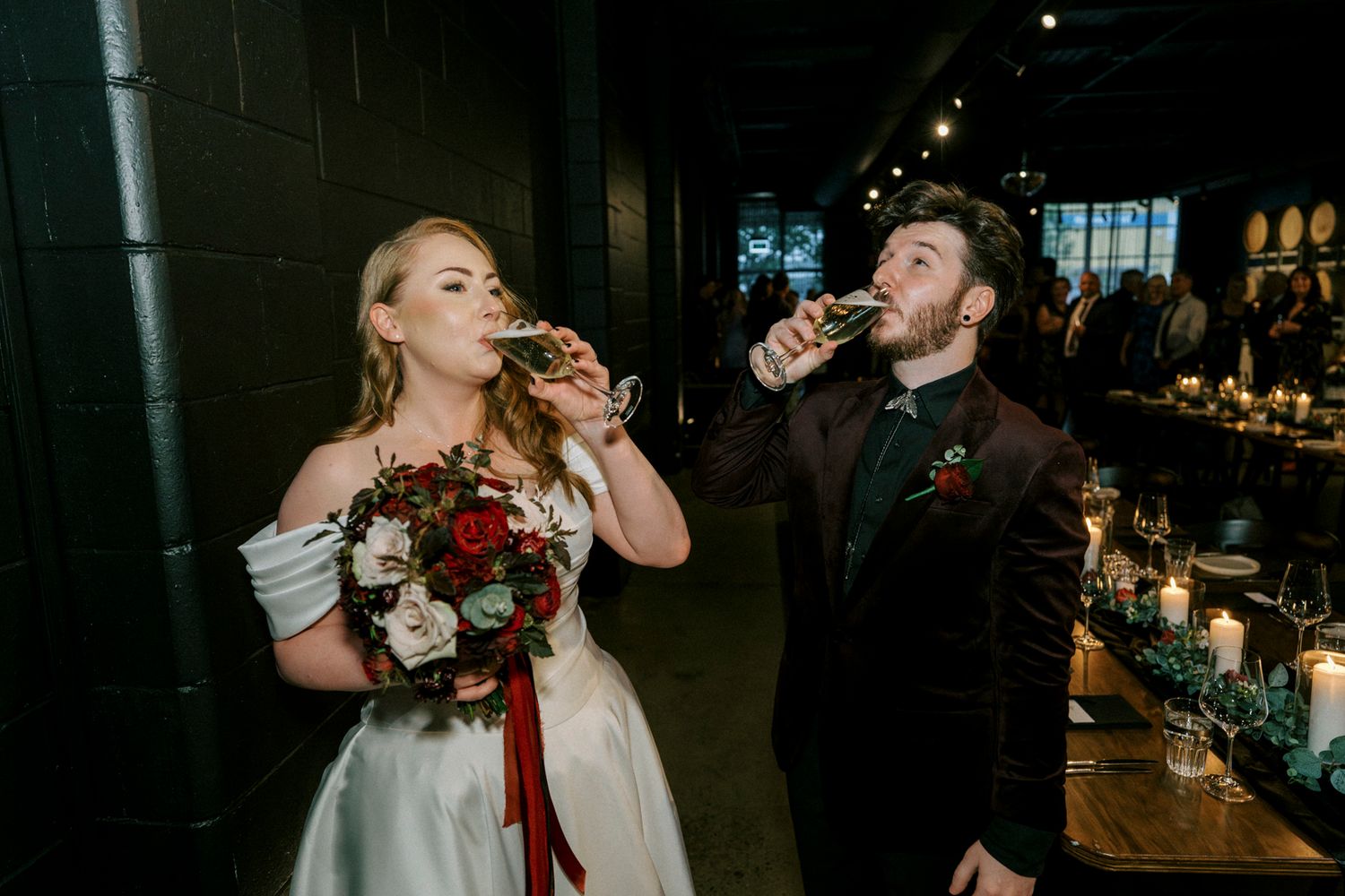 Bride and groom drinking champagne together at their wedding reception, bride holding red floral bouquet at the bethnal. Newstead Brisbane