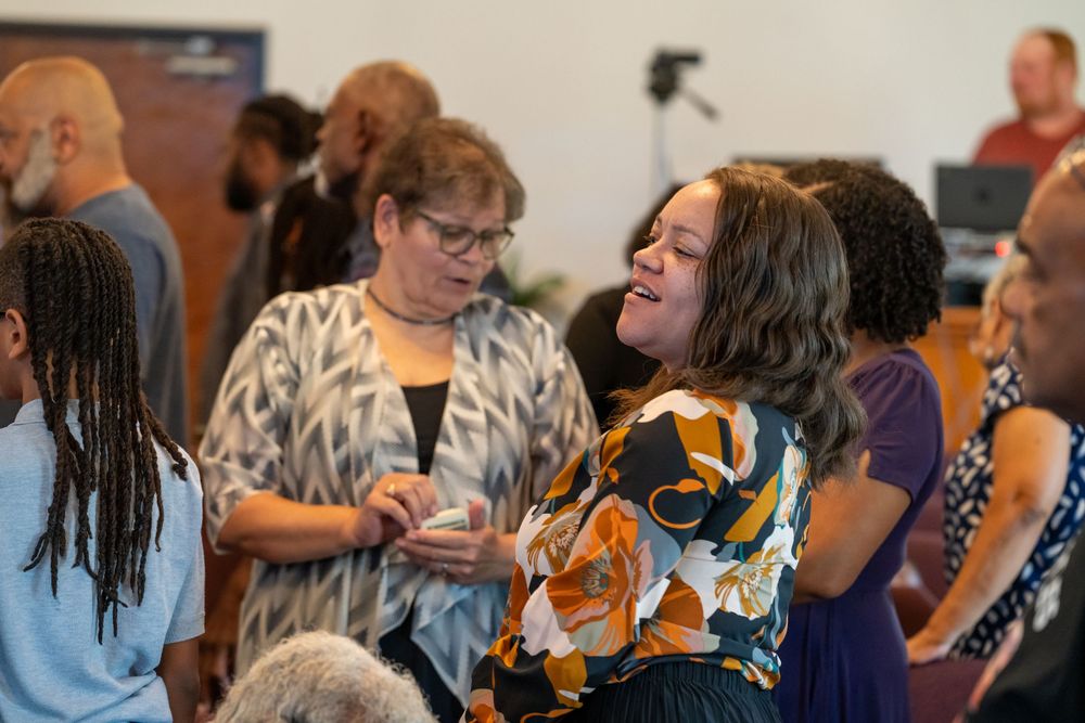 Two women smiling and conversing at a community gathering event in a bright indoor venue.