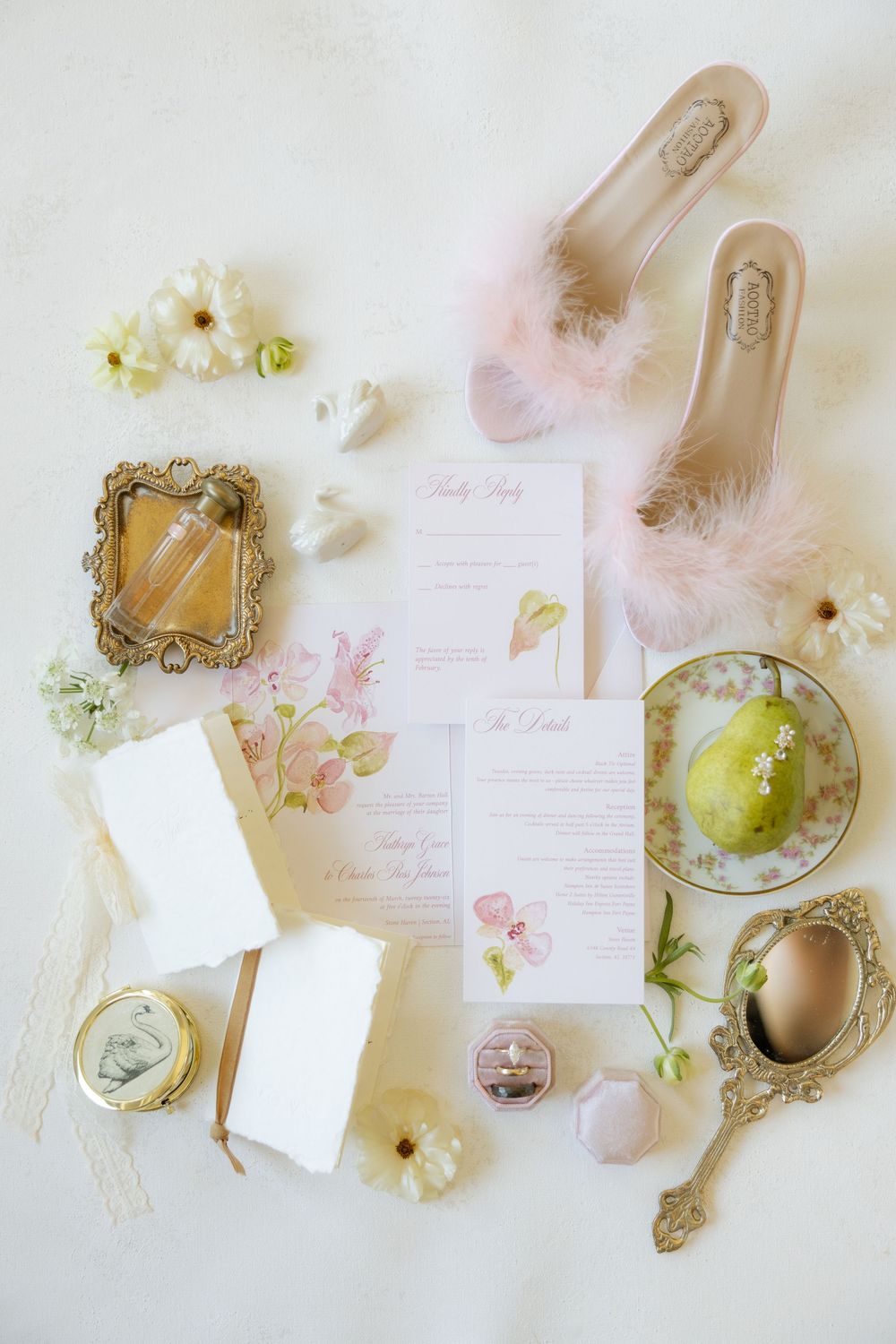 Elegant wedding flat lay with floral stationery, feather heels, vintage mirrors, and delicate blooms on white background.