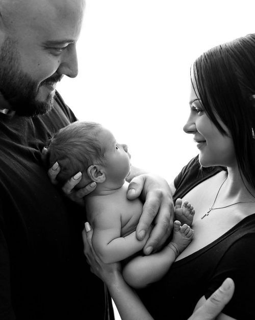 Black and white photo of smiling parents lovingly holding their newborn baby together.